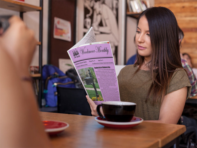 Person reading a newspaper in a café, with a coffee cup on the table.